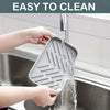 Hands are rinsing a silicone sink mat and organizer under running water in a kitchen sink.
