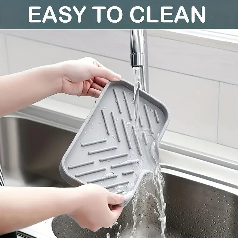 Hands are rinsing a silicone sink mat and organizer under running water in a kitchen sink.