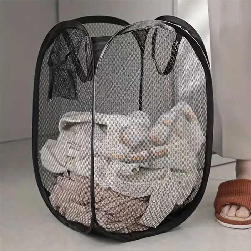 A black mesh pop-up laundry basket filled with folded white and beige clothing.