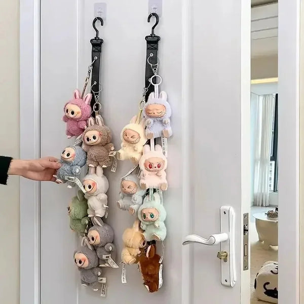 A hand hangs a collection of Labubu plush toys from a display artifact storage rack on a white door.