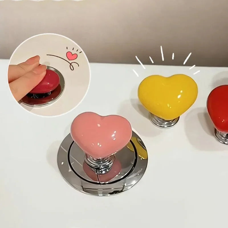 A collection of heart-shaped toilet presser buttons in pink, yellow, and red are displayed on a white surface.