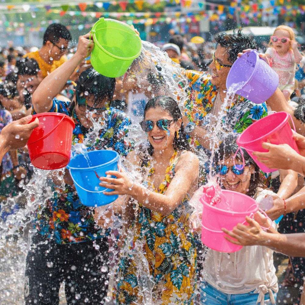 A group of people joyfully splashing water with six colorful plastic buckets outdoors.