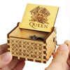 An antique wooden hand crank music box with intricate wood carving and a lid displaying the word QUEEN