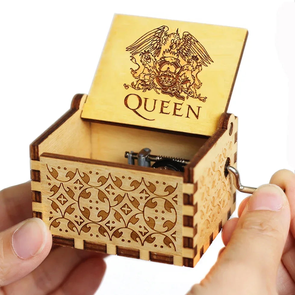 An antique wooden hand crank music box with intricate wood carving and a lid displaying the word QUEEN