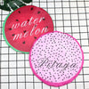 Two reusable fruit shower caps, one red with water melon text and one pink with Pitaya text, are displayed on a black grid ba