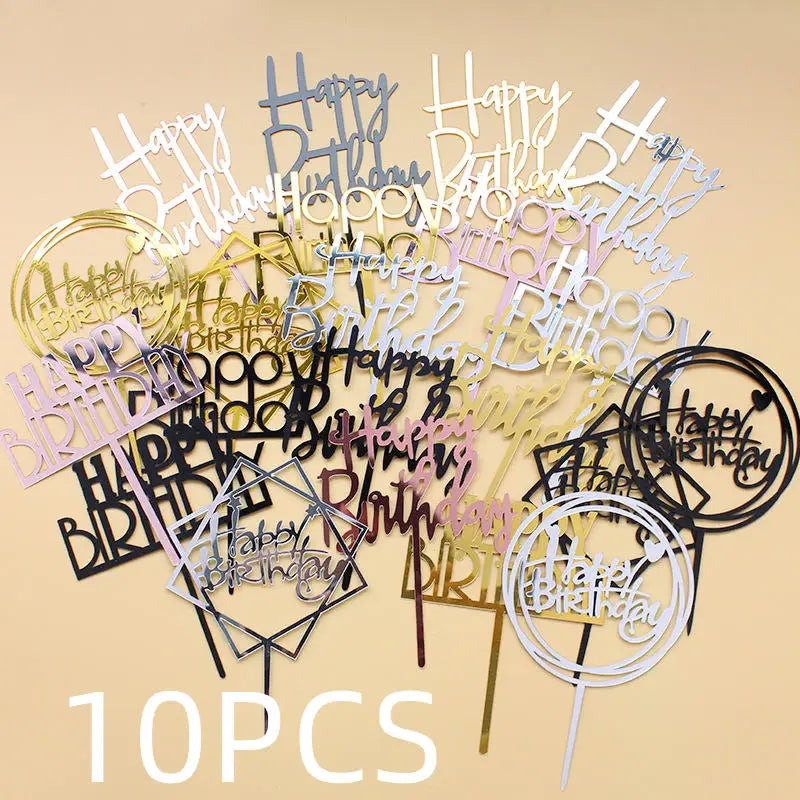 A collection of ten glittery acrylic birthday cake toppers in various fonts and styles scattered on a light background.