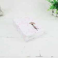 Un album photo rose avec de petites décorations florales repose sur une surface en bois blanc.