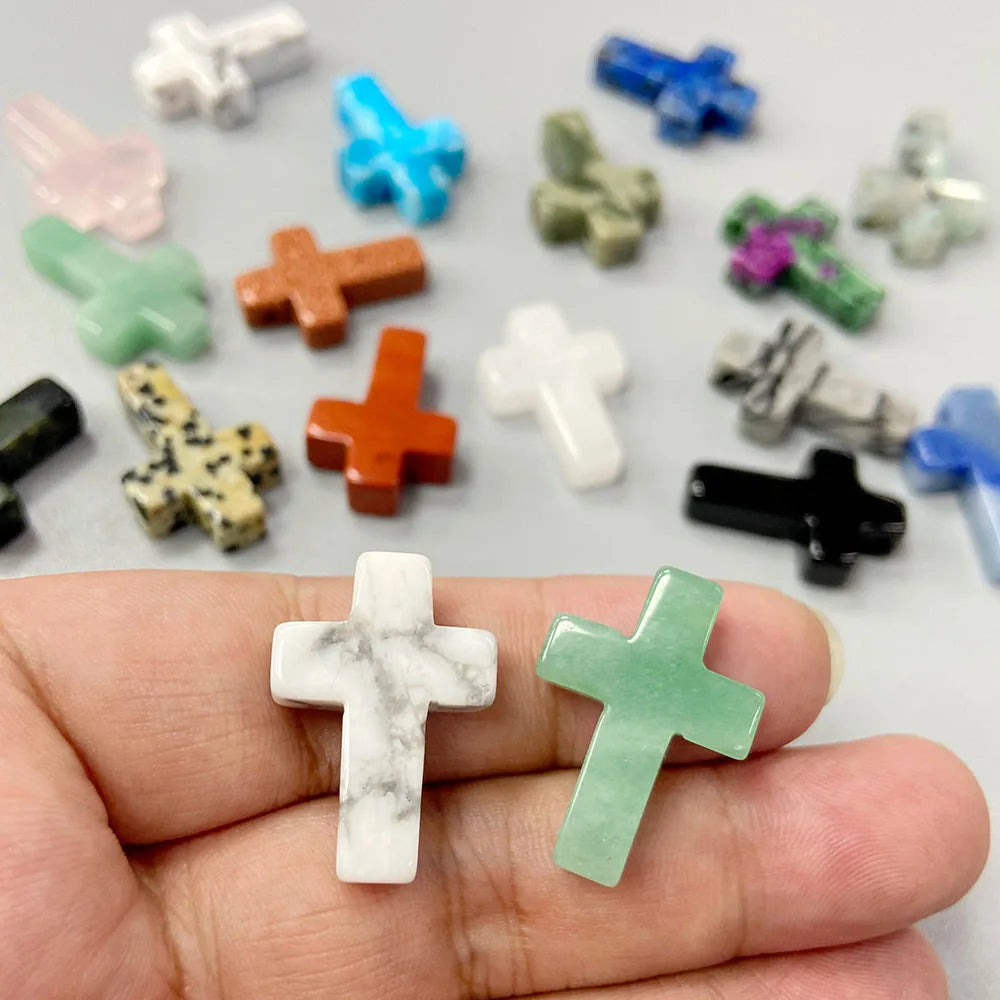 A hand holds a natural agate and jasper cross pendant charm surrounded by various colored gemstone charms.