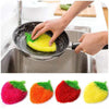 A hand is using a yellow strawberry scrubber sponge in a stainless steel sink for kitchen cleaning.