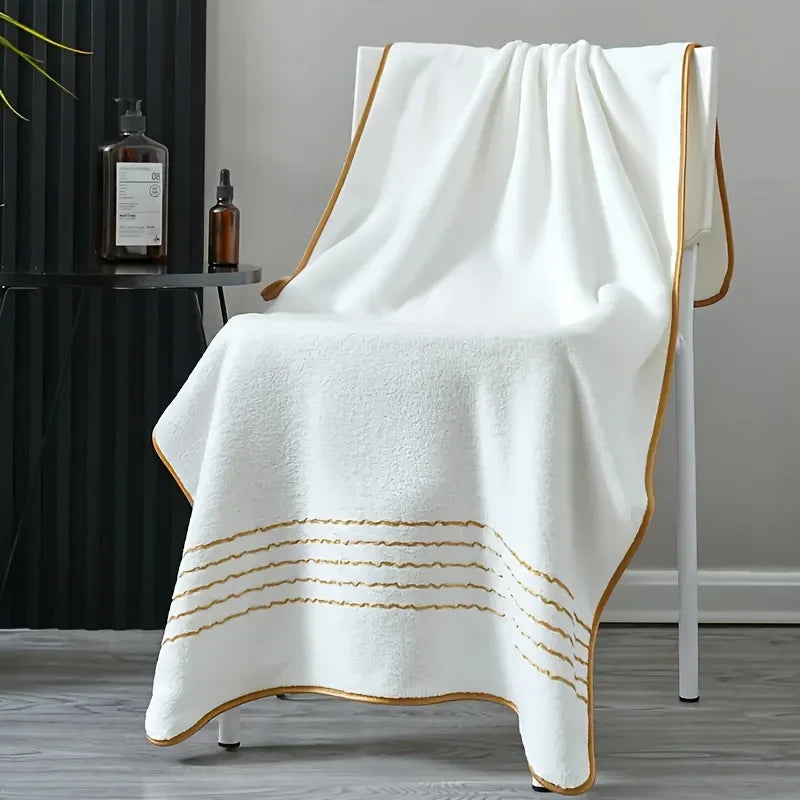 A white bath towel with gold stripes draped over a modern stand.