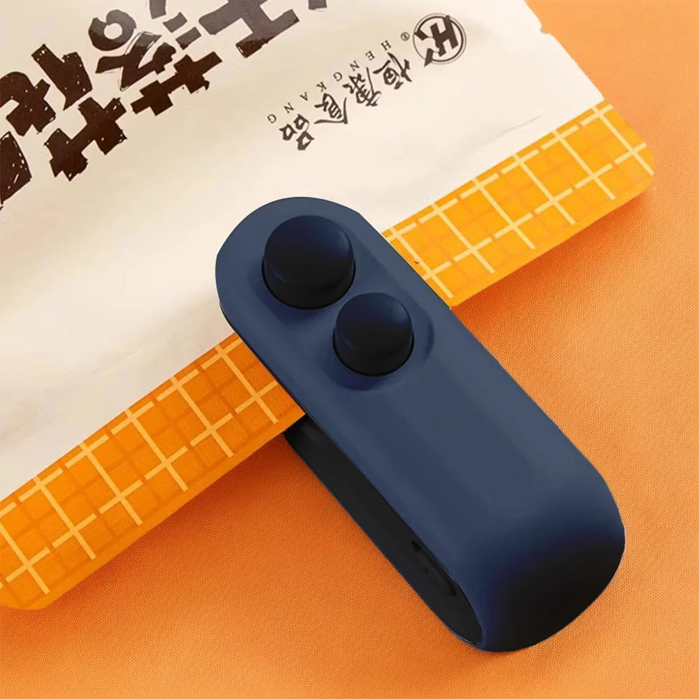 A dark blue handheld bag sealer and cutter tool rests on an orange surface next to a piece of white paper.