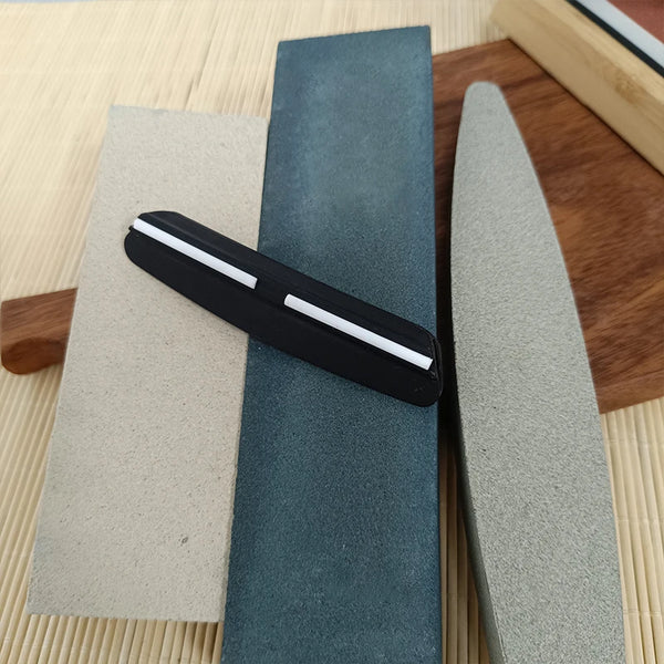 A set of multi-grit knife sharpening stones, including a black and white stone and a gray stone, resting on a wooden surface.