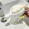 A hand is holding a white duck soap dish with a creamy white soap bar, positioned over a sink.