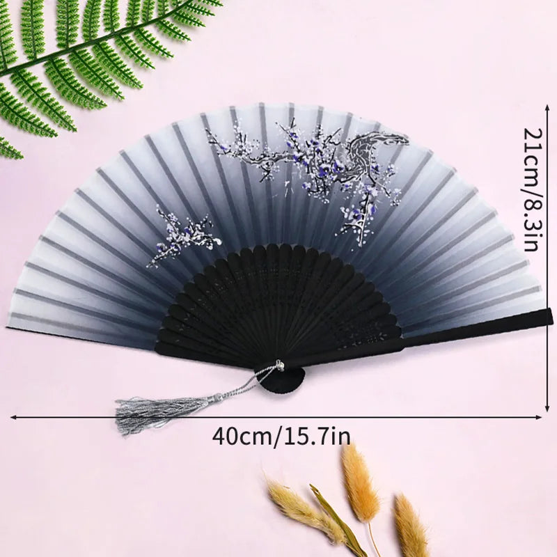 A black and silver lace fabric folding hand fan displayed against a pink background with green foliage.