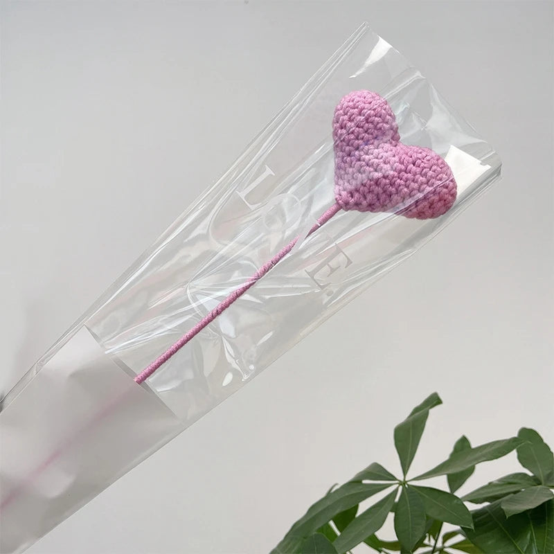 Un bouquet de cœurs en coton rose fait à la main, présenté dans une gaine en plastique transparent.