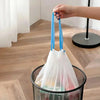 A hand is holding a blue drawstring trash bag over a black mesh basket.