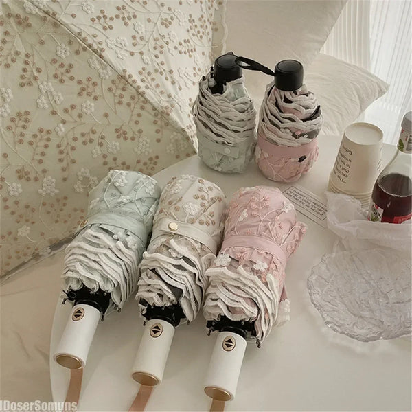 A set of full-automatic embroidered sun umbrellas in white and pink fabric are displayed on a white surface.