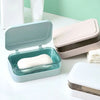 A light blue transparent drainage soap dish holding a white bar of soap on a white surface.