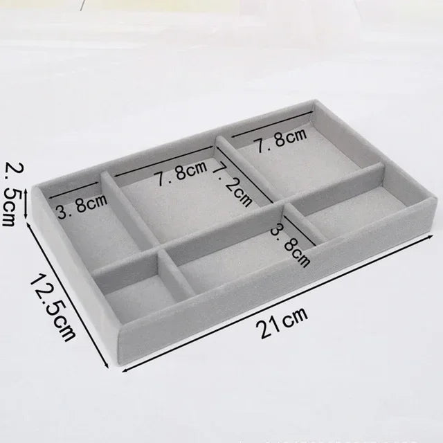 A rectangular gray velvet jewelry organizer tray divided into six compartments with various sized sections.