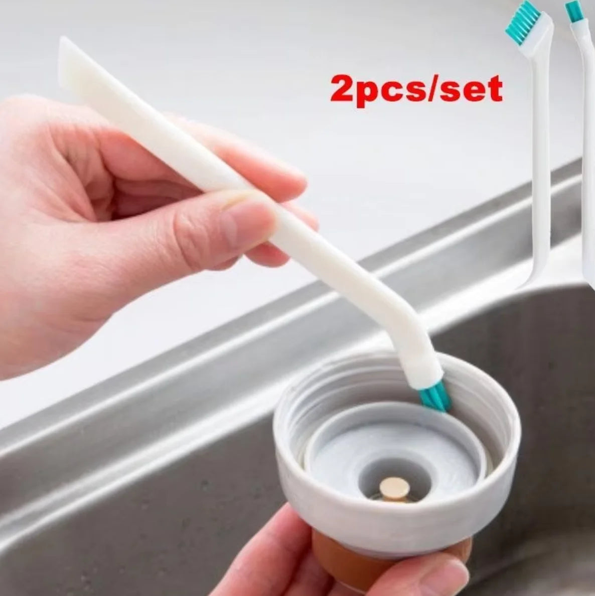 A hand is using a white dual-sided silicone cleaning brush set to clean a bottle inside a stainless steel sink.