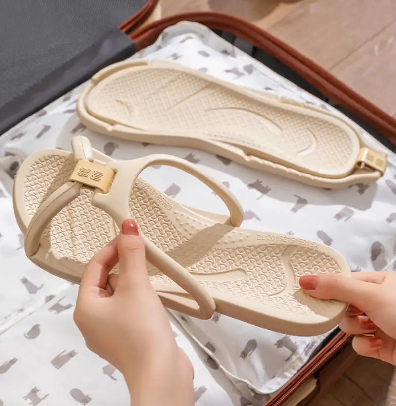 Une main tient une sandale EVA pliable beige sur une surface de tissu blanc.