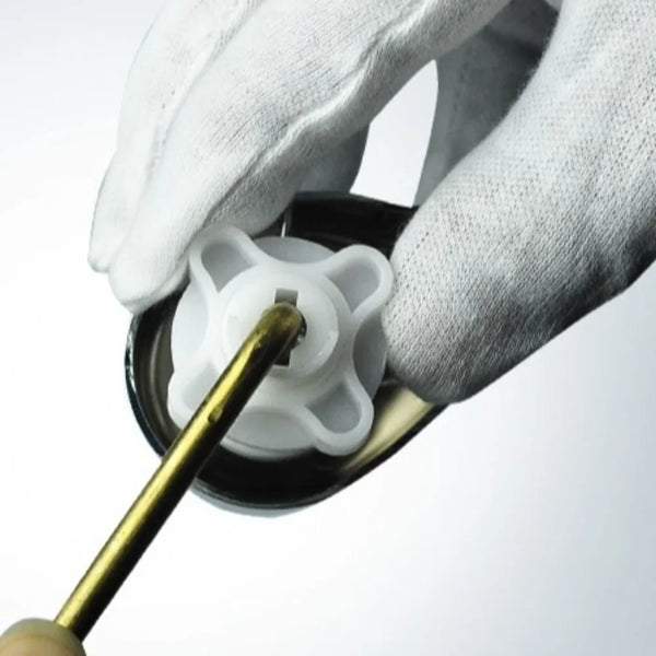 A hand wearing a white glove is operating the flush lever of a brass side mount toilet.