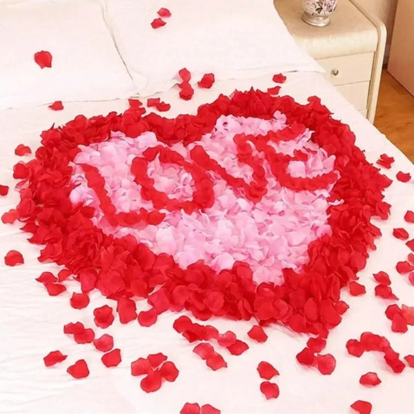 A heart shape made of red and pink artificial rose petals spread on a white bed.