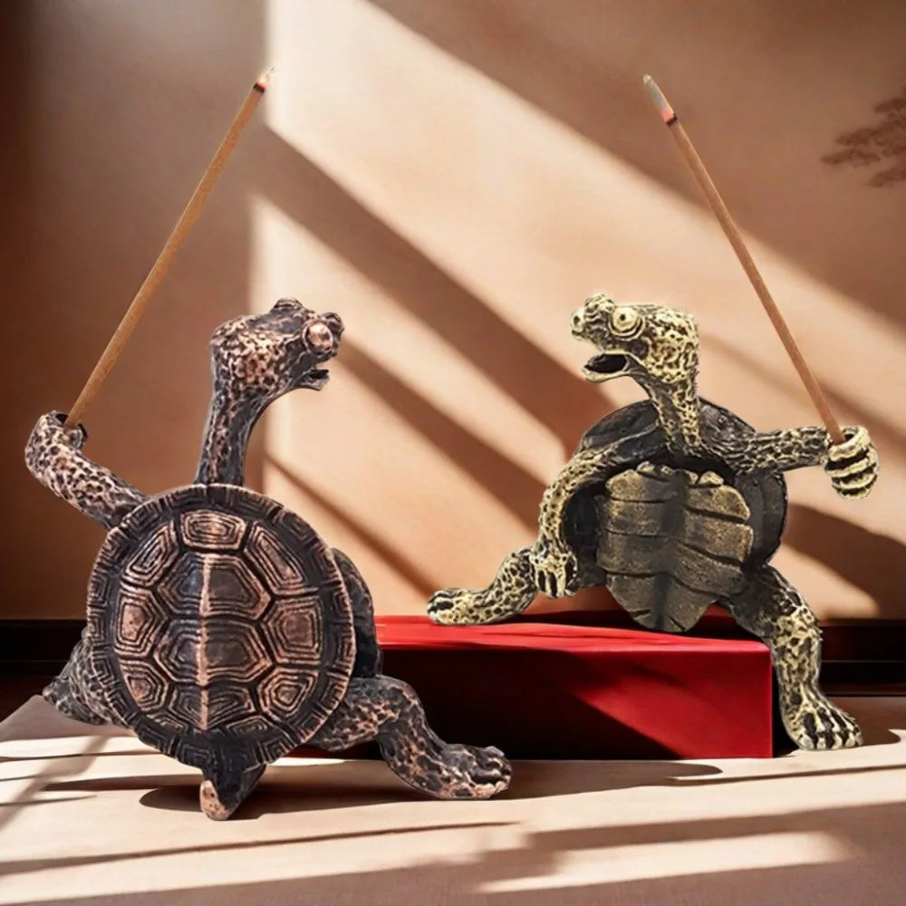 Petite figurine de tortue en métal avec une perche, contre un fond clair avec des ombres.