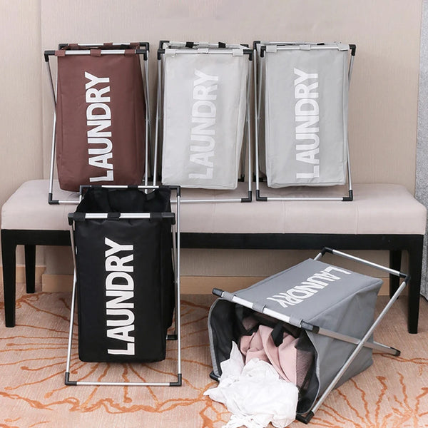 Three foldable laundry baskets in brown, white, and black are displayed on a table.