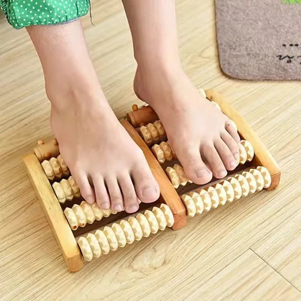 A pair of feet is resting on a wooden foot massage roller with small wooden rollers.