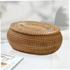 A round, woven rattan storage basket with a matching lid resting on a white surface.