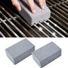 A hand is using a gray pumice stone or brush to clean the grates of a BBQ grill.