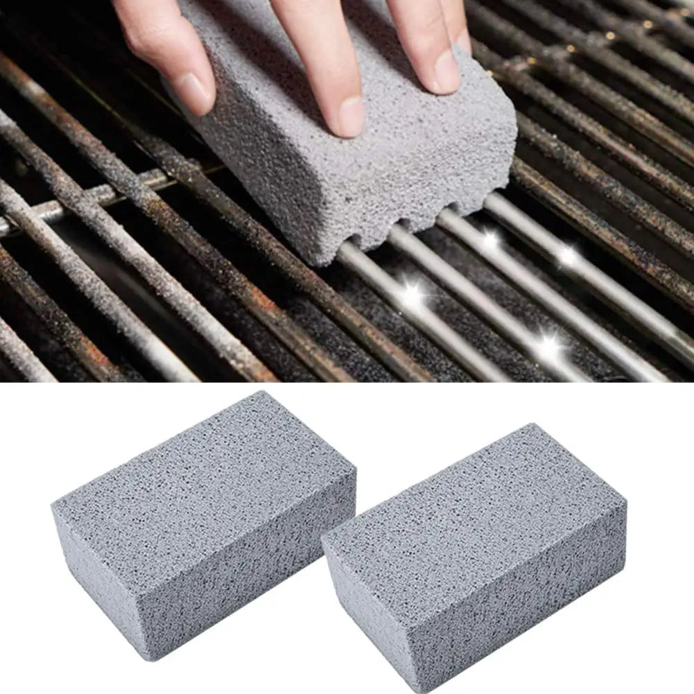 A hand is using a gray pumice stone or brush to clean the grates of a BBQ grill.