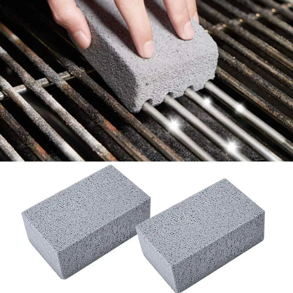 A hand is using a gray pumice stone or brush to clean the grates of a BBQ grill.