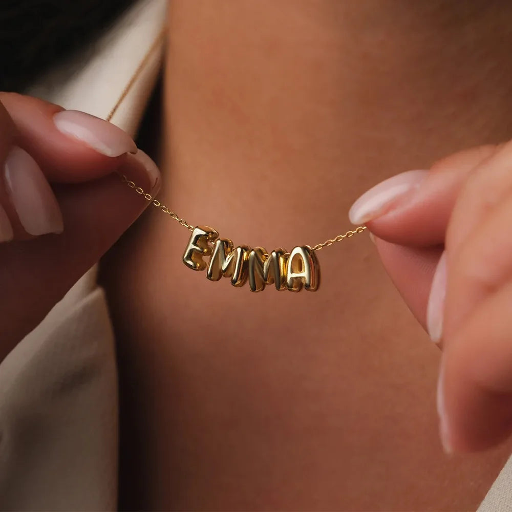 Nahaufnahme einer vergoldeten 3D-Blasenbuchstaben-Kette mit dem Namen EMMA, getragen um den Hals.