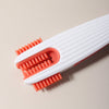 A silicone baby bottle cleaning set with white and orange bristles shown diagonally on a light background.