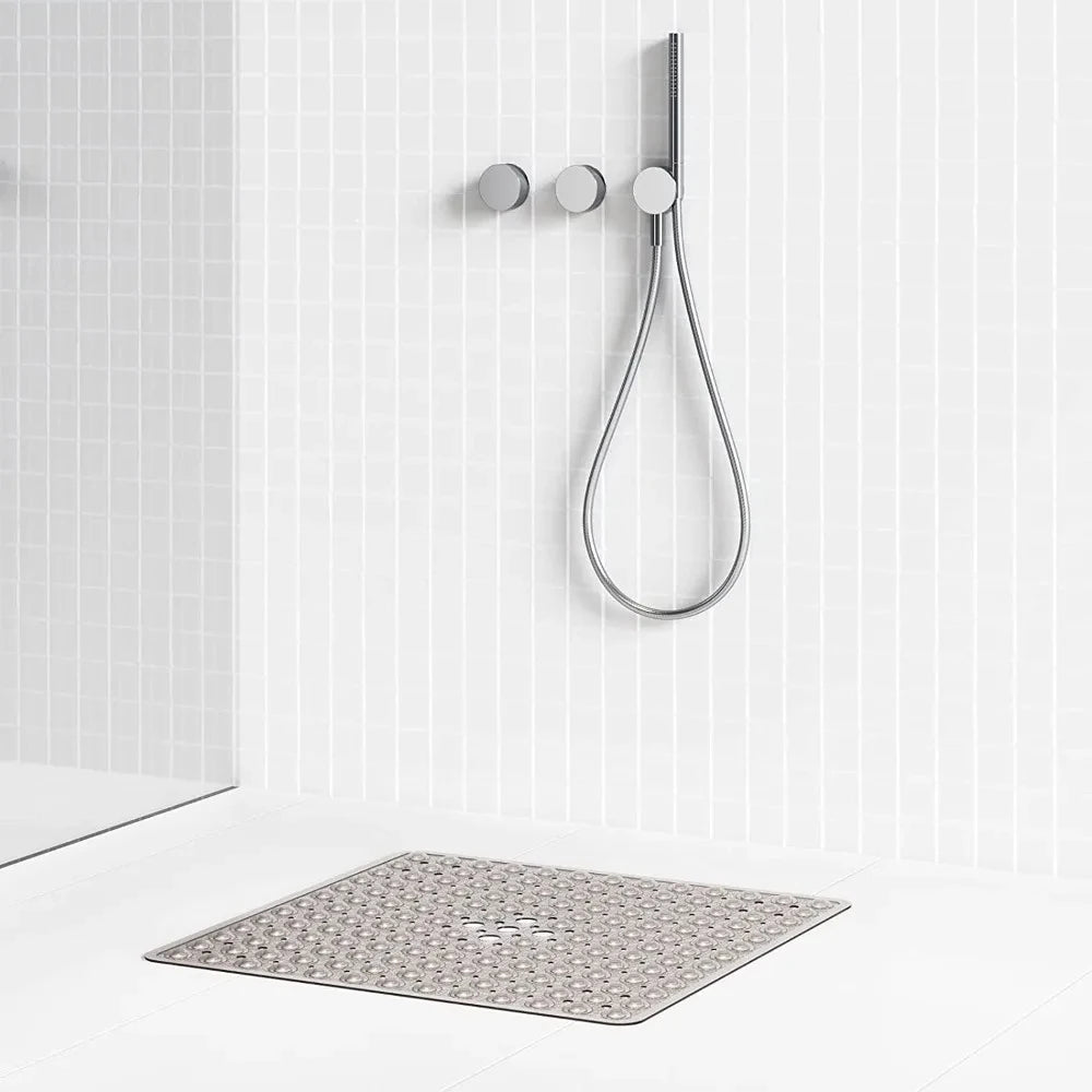 A silver non-slip shower mat with suction cups hangs on a white tiled wall.