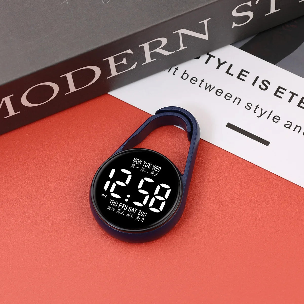 A dark blue digital LED hanging pocket watch displaying 12:58 on a red surface.