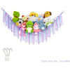 A colorful bohemian stuffed animal hammock featuring various plush toys hanging from purple and pink strings.