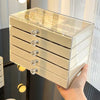 A clear acrylic 5-tier desktop jewelry organizer rack with gold accents is being held by a hand.