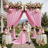 Cortinas de tela rosa enmarcando a una pareja y arreglos florales para un evento al aire libre.
