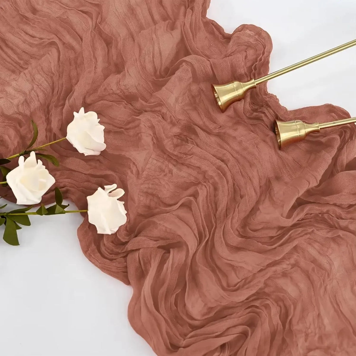 A set of boho cheesecloth table runners in a dusty rose color with gold-toned metal accents and white floral sprigs.