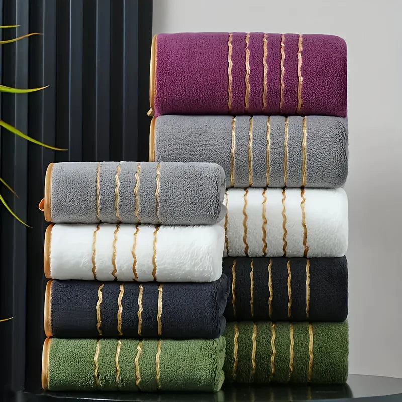 A stack of various colored bath towels, including purple, gray, white, black, and olive green.