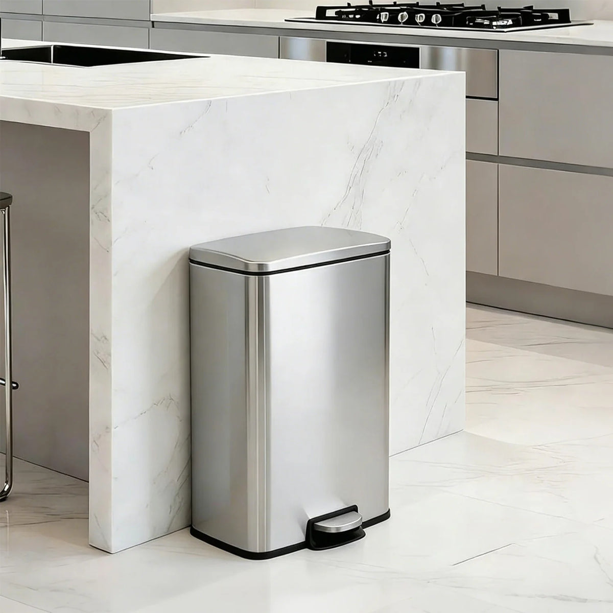 A stainless steel pedal trash bin sitting on a white marble kitchen countertop.