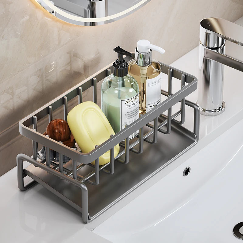 Stainless steel kitchen sink caddy with drainage tray holding various cleaning bottles and a yellow sponge