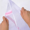 A hand is holding a white mesh laundry bag with a pink elastic closure.