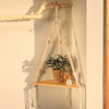 A boho triangle floating wall shelf made of natural twine and wood, holding a potted green plant.