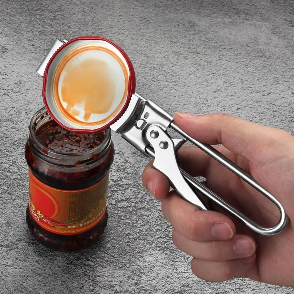 A hand holds a stainless steel multi-function can opener, positioned next to a glass jar of preserved food with its lid open.
