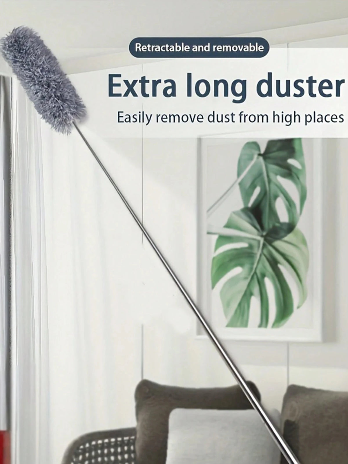 A long, retractable duster brush with a fluffy head is shown next to a potted plant in a bright room.