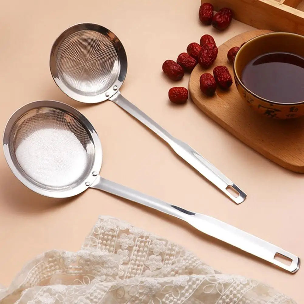 Stainless steel fat skimmer strainer spoon resting on a wooden board with red berries and a cup